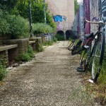 Corridoio con panchine infestate da erbacce e biciclette abbandonate